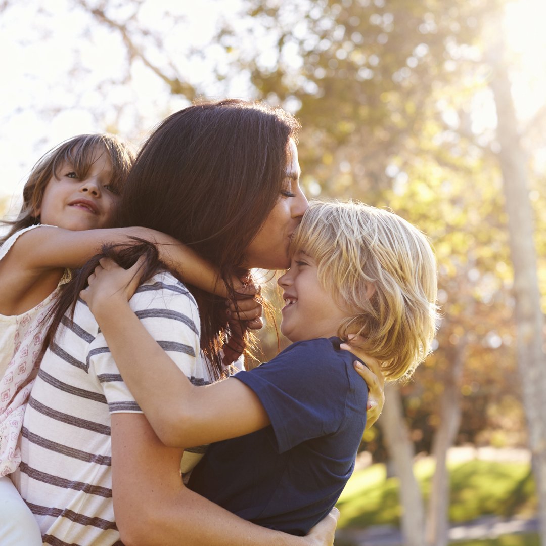 mother outside, holding two youths, kissing one on the forehead